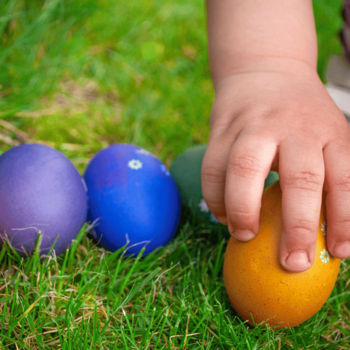 Chubby toddler hand picking up an egg during an Easter egg hunt
