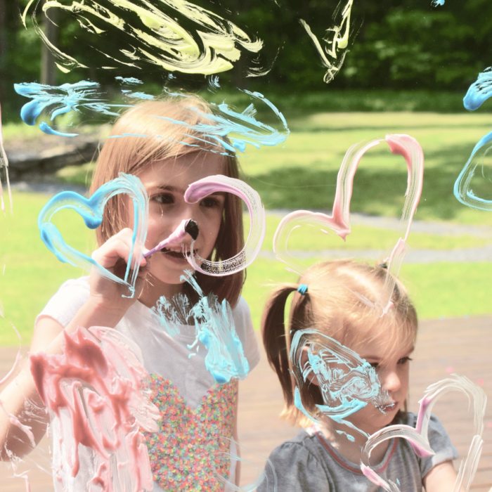 Kids painting a window with colored shaving cream.