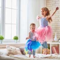 Sisters wearing tutus jumping on the bed together