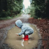 Boy wearing rain boots playing in a puddle