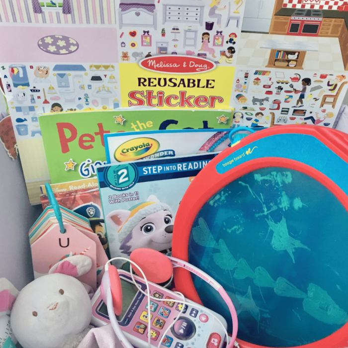 A basket of toddler activities for the car- sticker books, lovey blanket, audio player and boogie board.