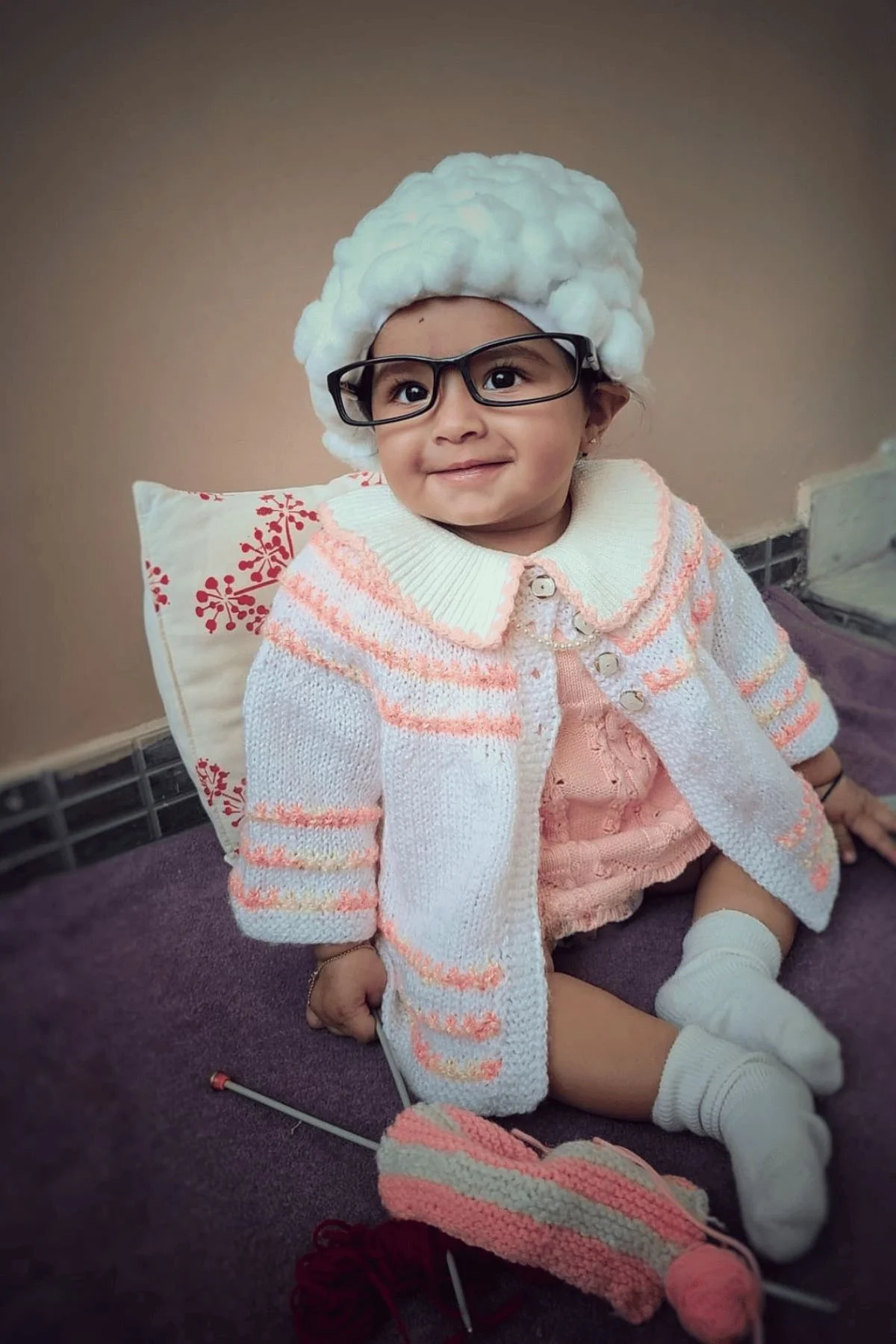 Baby with cotton ball hair, sweater and knitting yarn