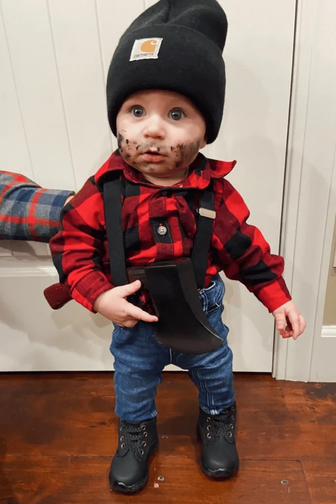 Baby wearing a Carhart hat, plaid shirt, jeans, boots and holding an axe