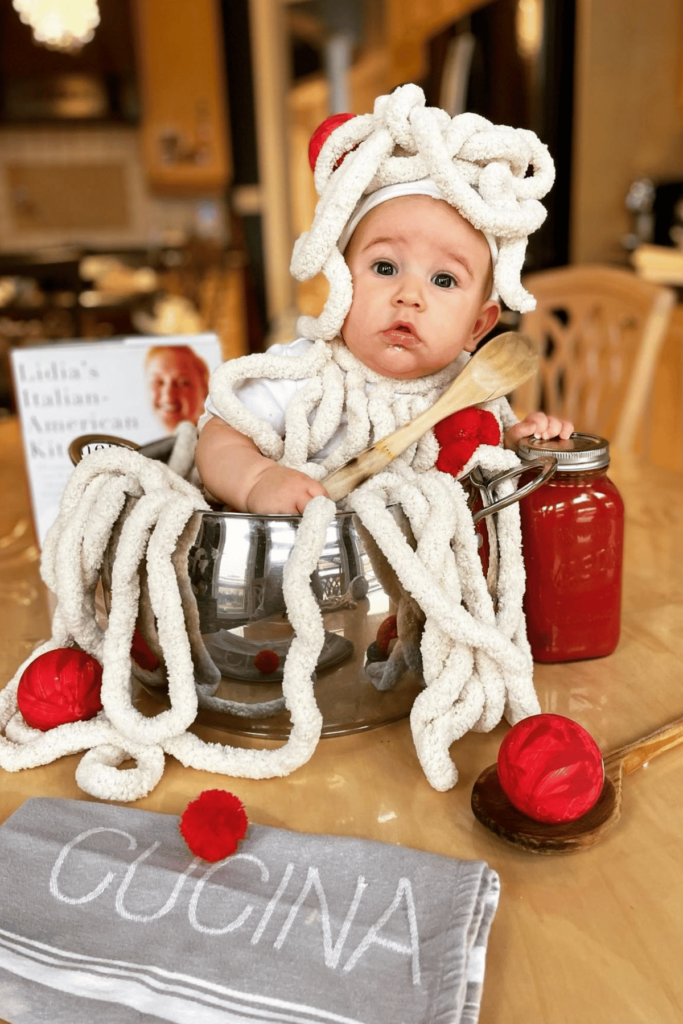 Baby in a pot with thick yarn spaghetti and red pom pom meatballs