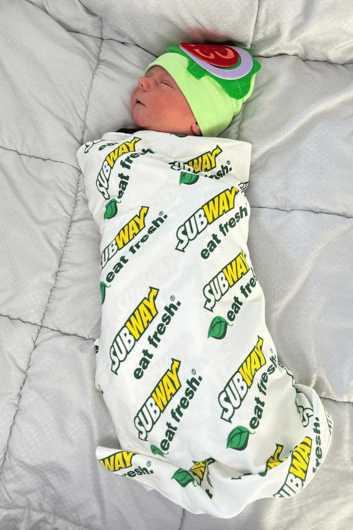 Baby wrapped in a subway sub swaddle with a hat with felt tomato and lettuce