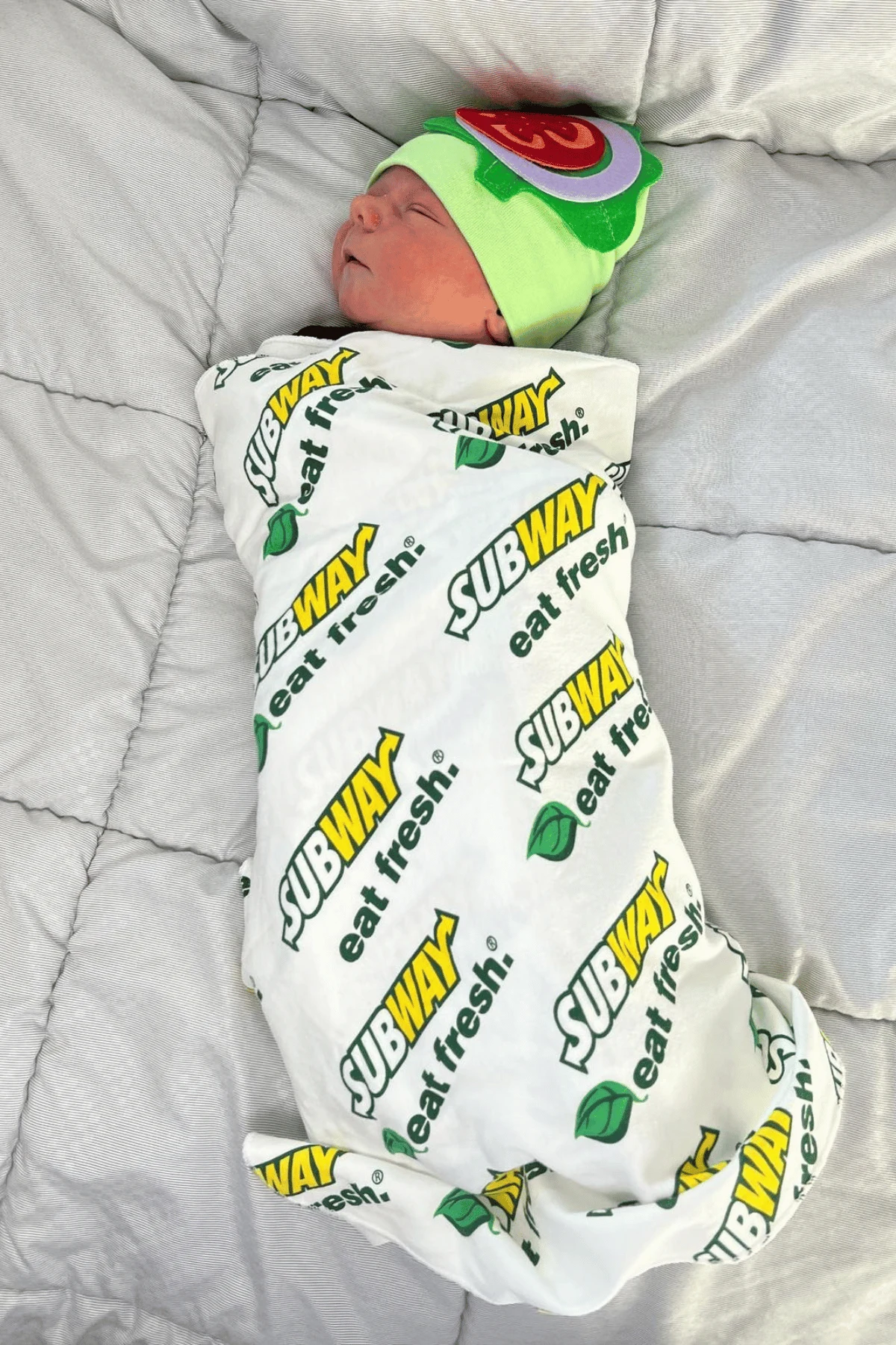 Baby wrapped in a subway sub swaddle with a hat with felt tomato and lettuce