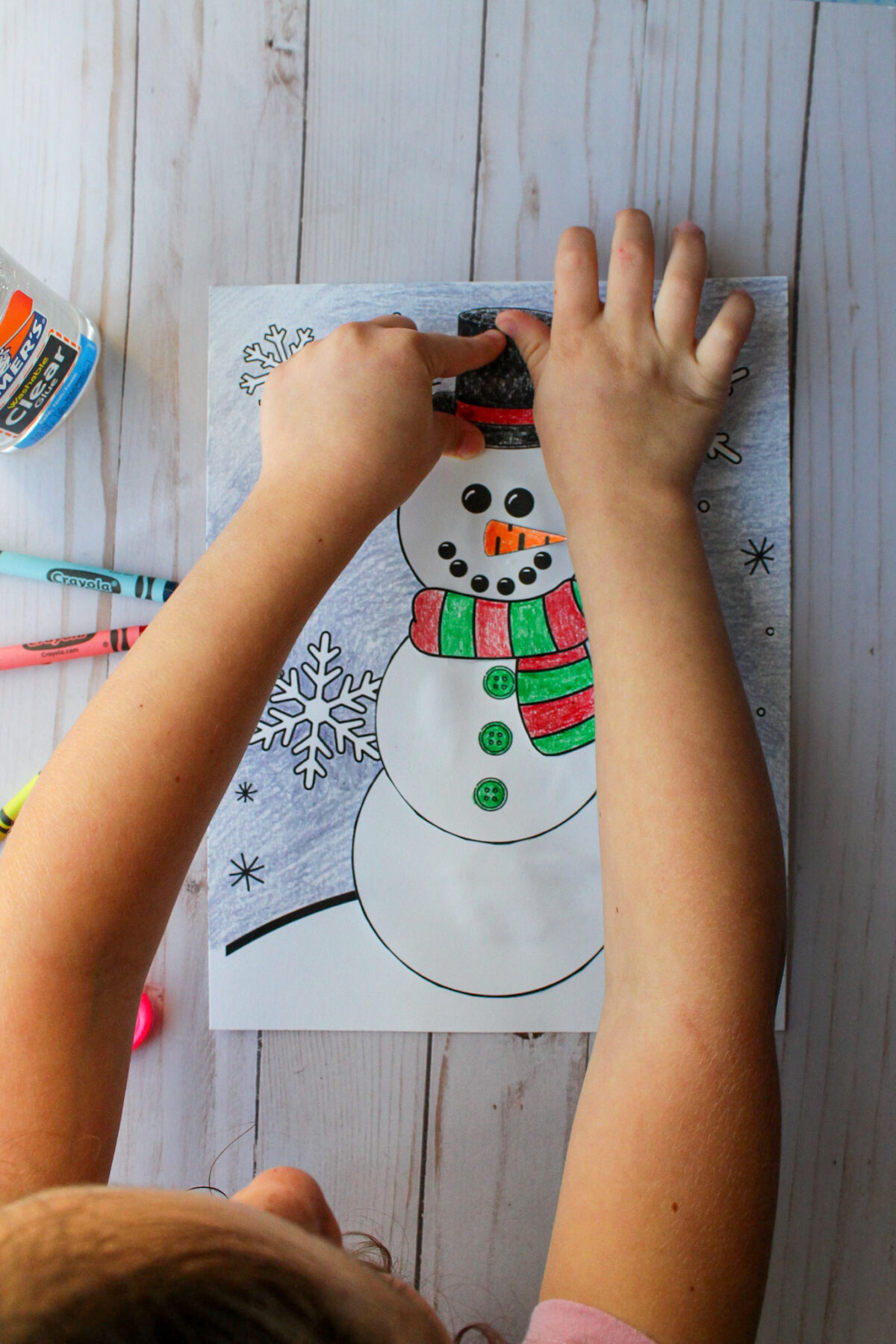 Girl pasting the snowman's hat onto the snowman