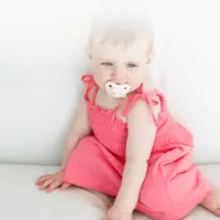 Baby girl sitting and sucking on a pacifier